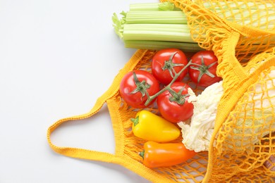 Photo of String bag with different vegetables on light grey background, top view