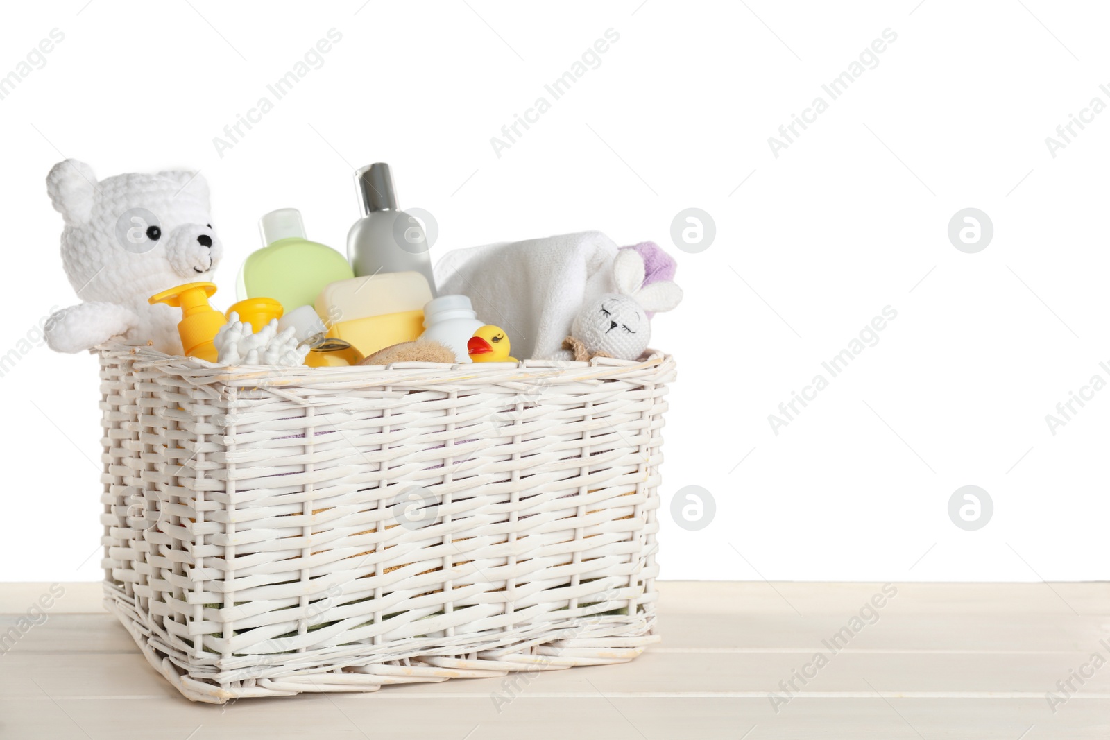 Photo of Wicker basket full of different baby cosmetic products, bathing accessories and toys on wooden table against white background