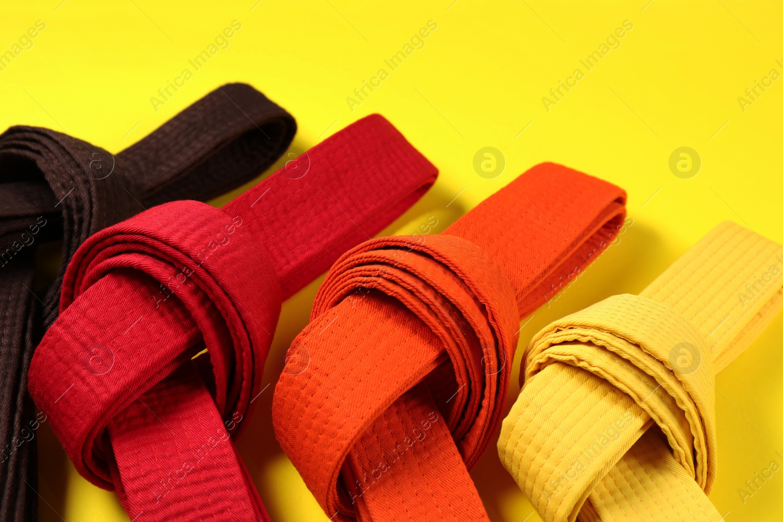 Photo of Colorful karate belts on yellow background, closeup