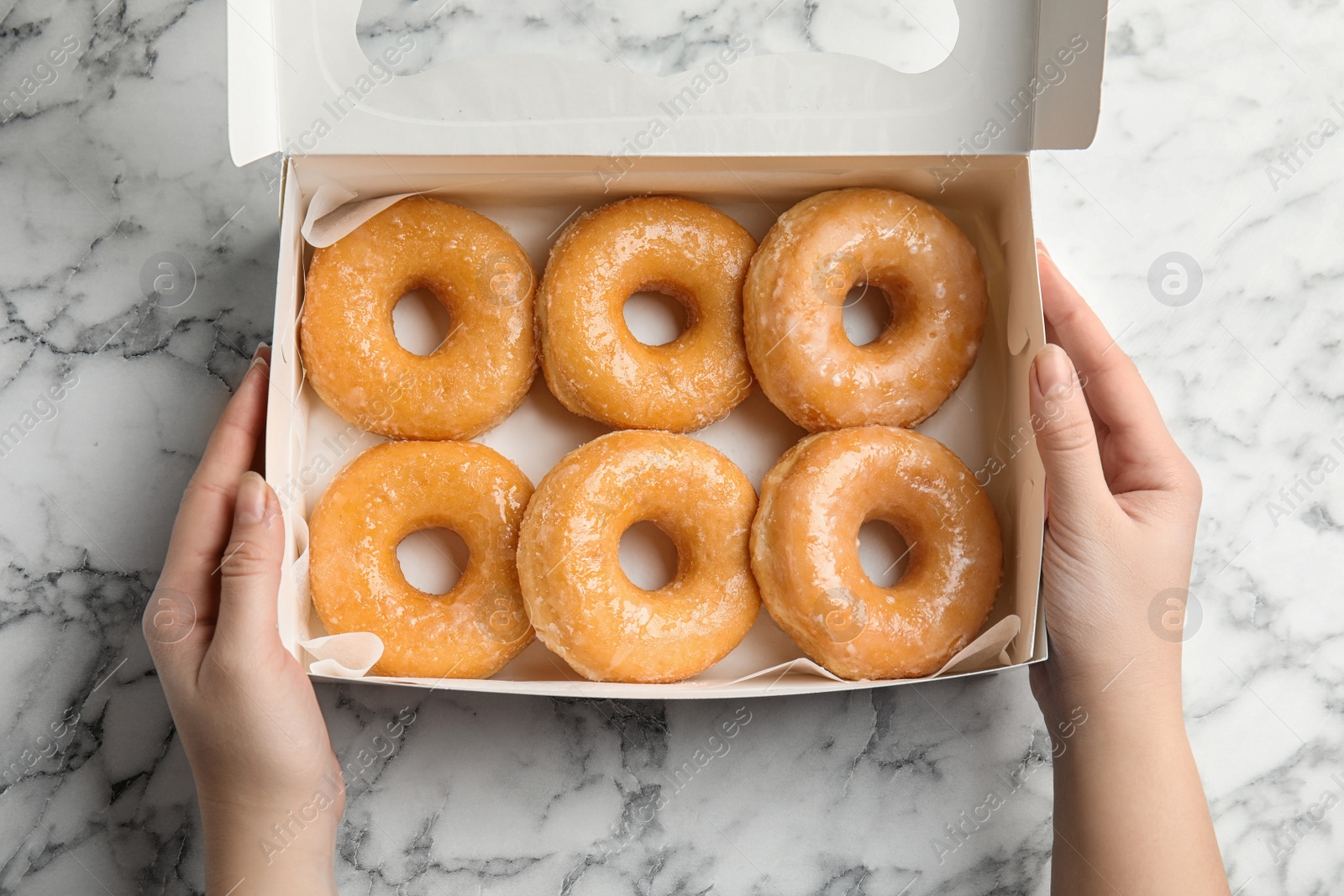 Photo of Woman with box of delicious donuts at marble table, top view