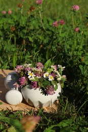 Photo of Ceramic mortar with pestle, different wildflowers and herbs on wooden board in meadow