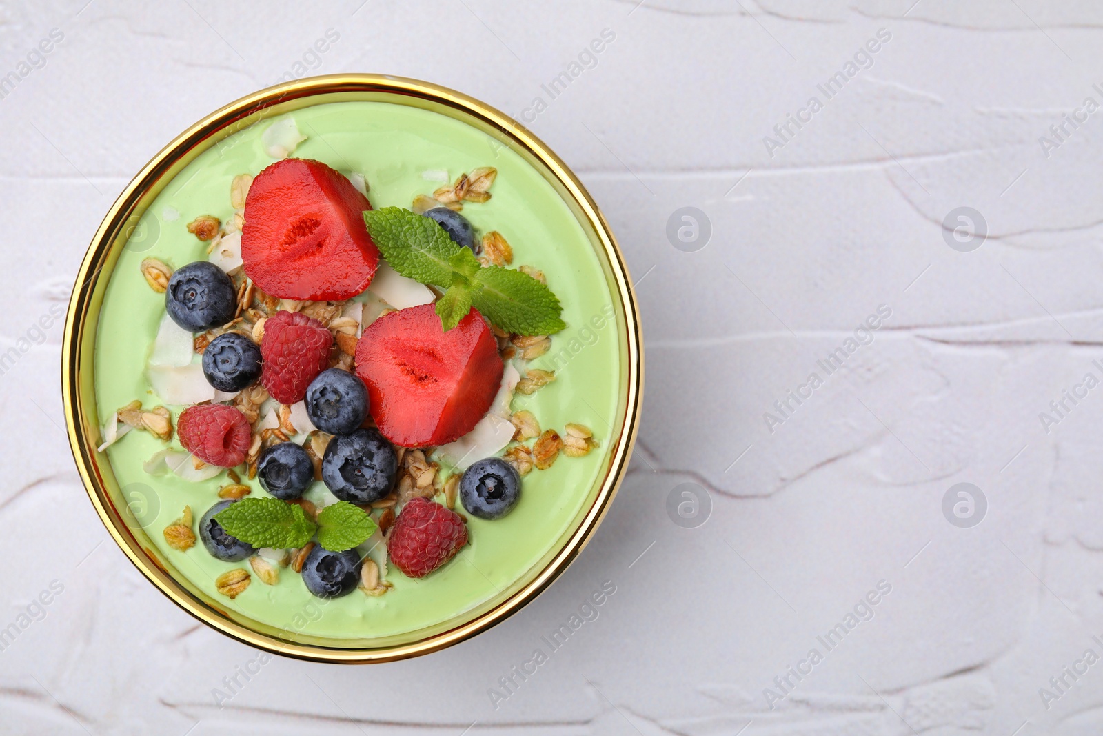 Photo of Tasty matcha smoothie bowl served with berries and oatmeal on white textured table, top view with space for text. Healthy breakfast