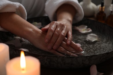 Photo of Woman soaking her hands in bowl of water and flower petals, closeup. Spa treatment