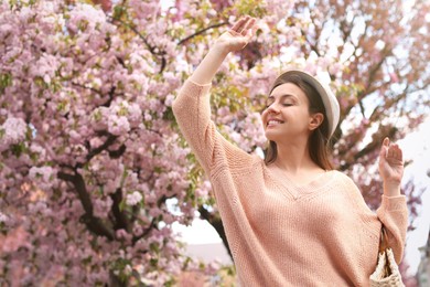 Photo of Happy stylish young woman near blossoming sakura tree outdoors. Spring look