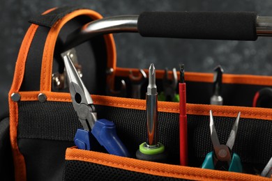 Photo of Bag with needle nose pliers, screwdrivers and other tools for repair on dark background, closeup