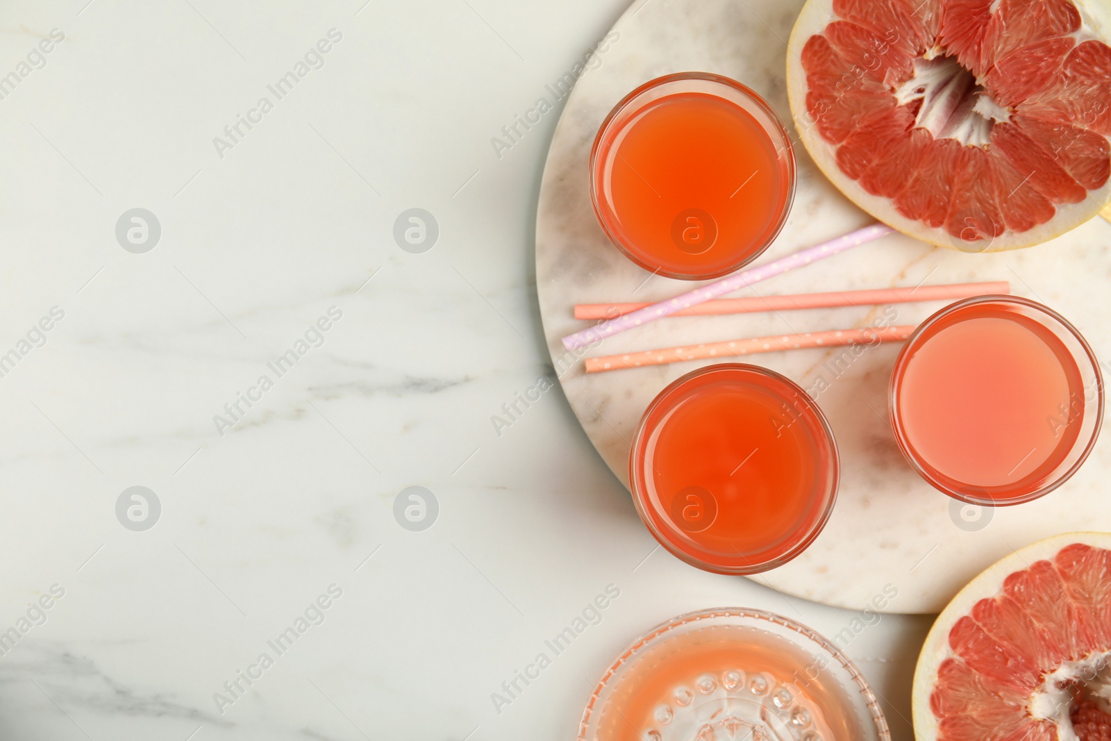 Photo of Glasses of pink pomelo juice with straws and fruit on white marble table, flat lay. Space for text