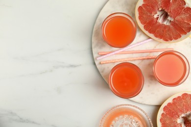 Photo of Glasses of pink pomelo juice with straws and fruit on white marble table, flat lay. Space for text