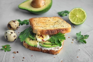 Photo of Crisp toast with sliced avocado, cream cheese and quail eggs on table, closeup