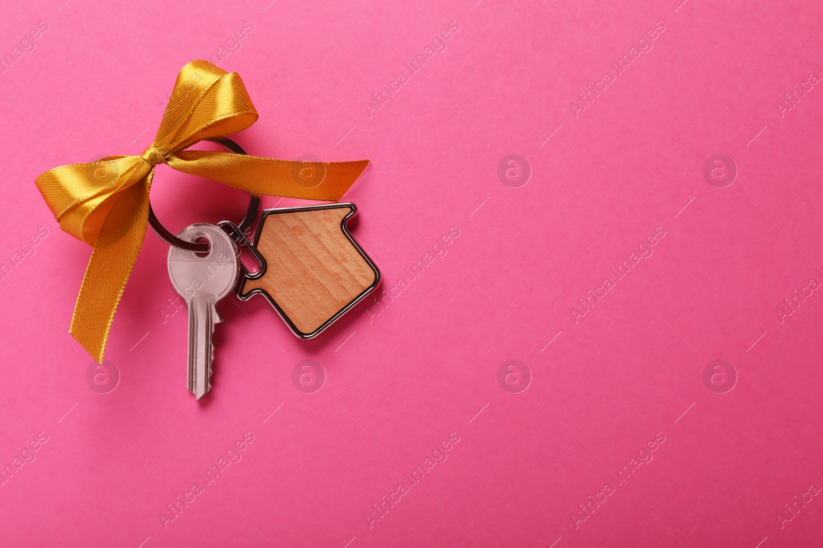 Photo of Key with trinket in shape of house and bow on pink background, top view. Space for text. Housewarming party