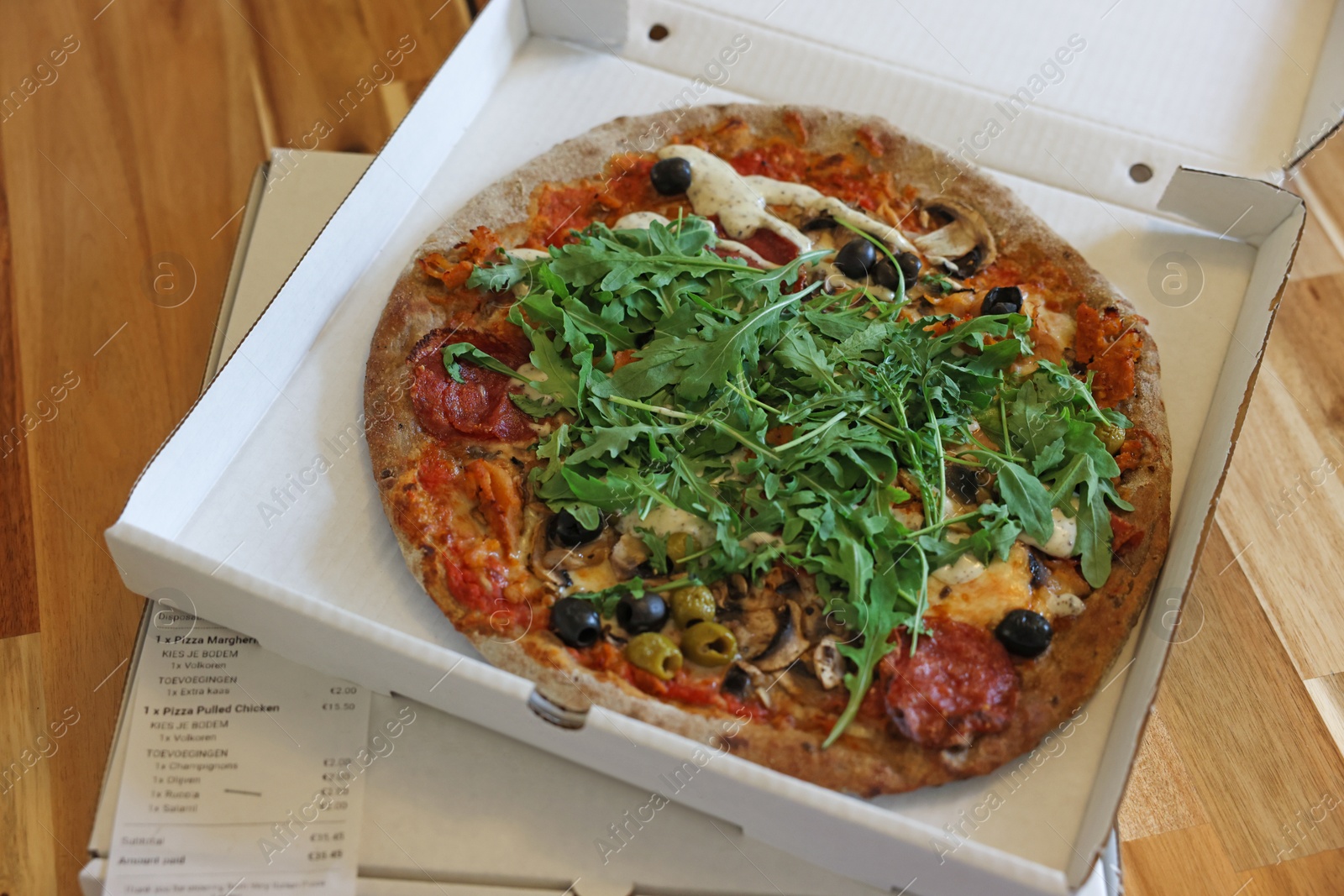 Photo of Delicious pizza with arugula, mushrooms and olives in box on wooden table