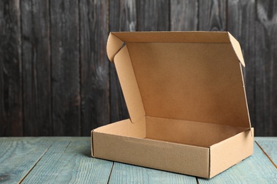 Photo of Cardboard box on light blue wooden table against dark background