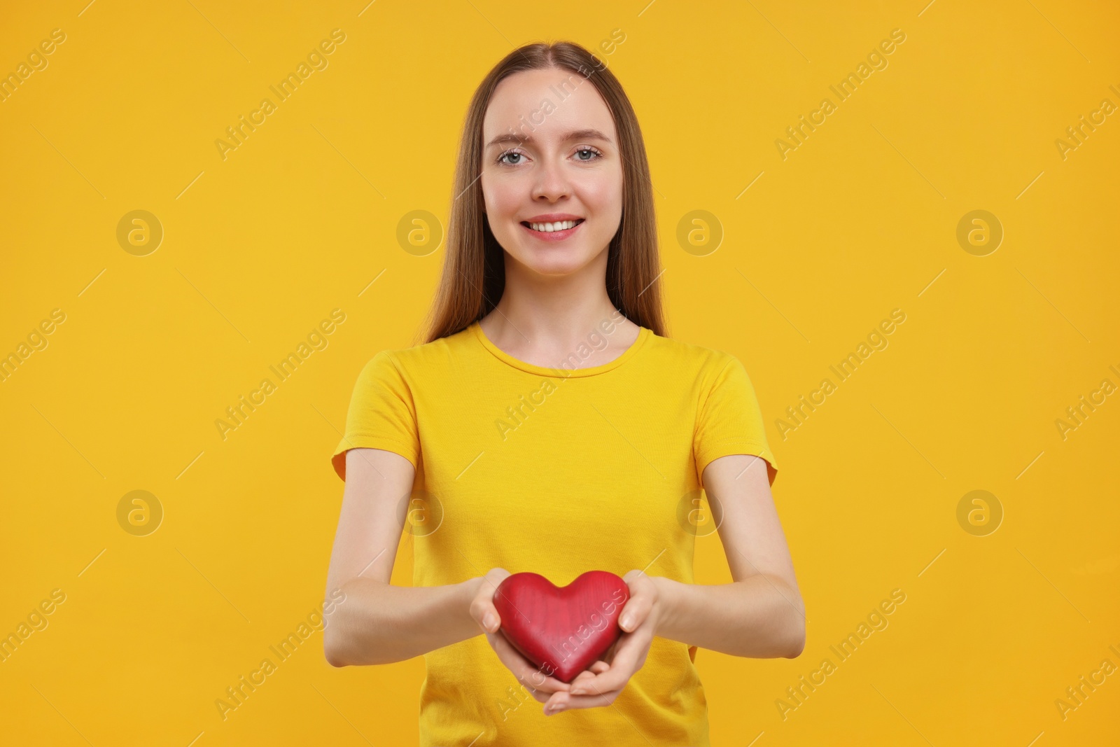 Photo of Happy young woman holding red heart on yellow background