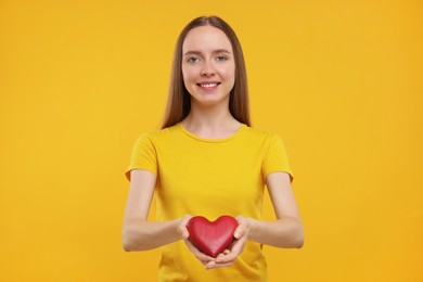 Photo of Happy young woman holding red heart on yellow background