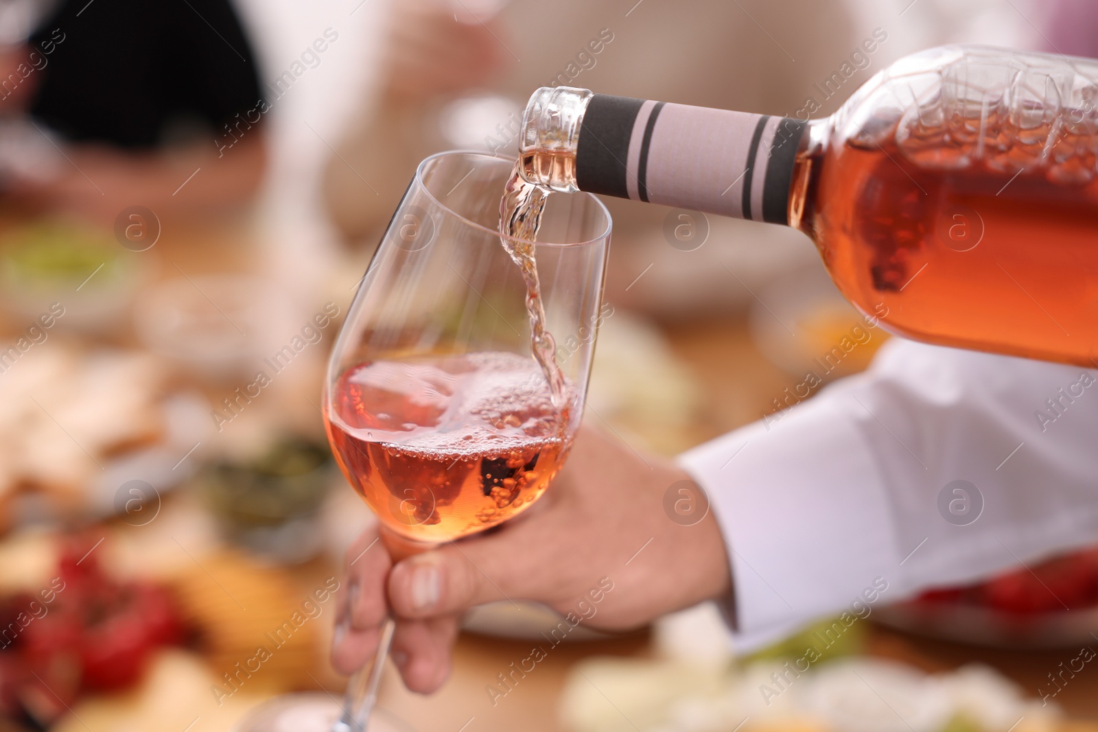 Photo of Man pouring rose wine from bottle into glass indoors, closeup