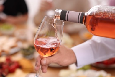 Man pouring rose wine from bottle into glass indoors, closeup