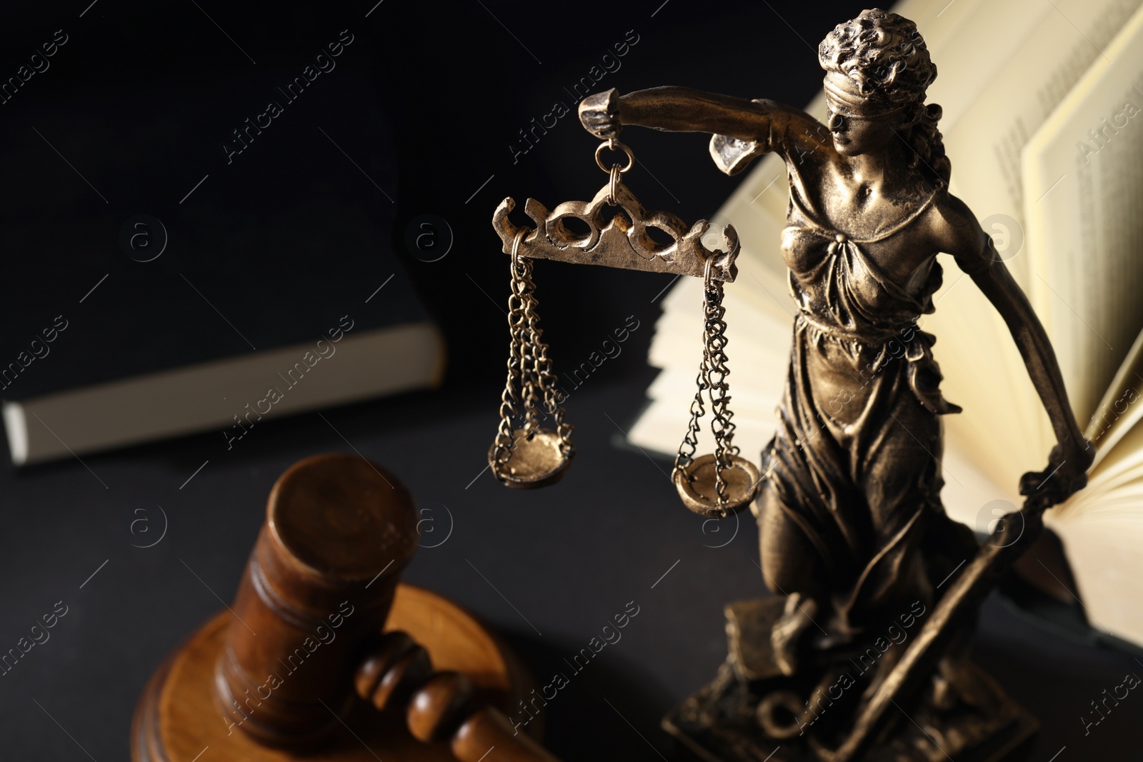 Photo of Symbol of fair treatment under law. Statue of Lady Justice near gavel and open book on black table