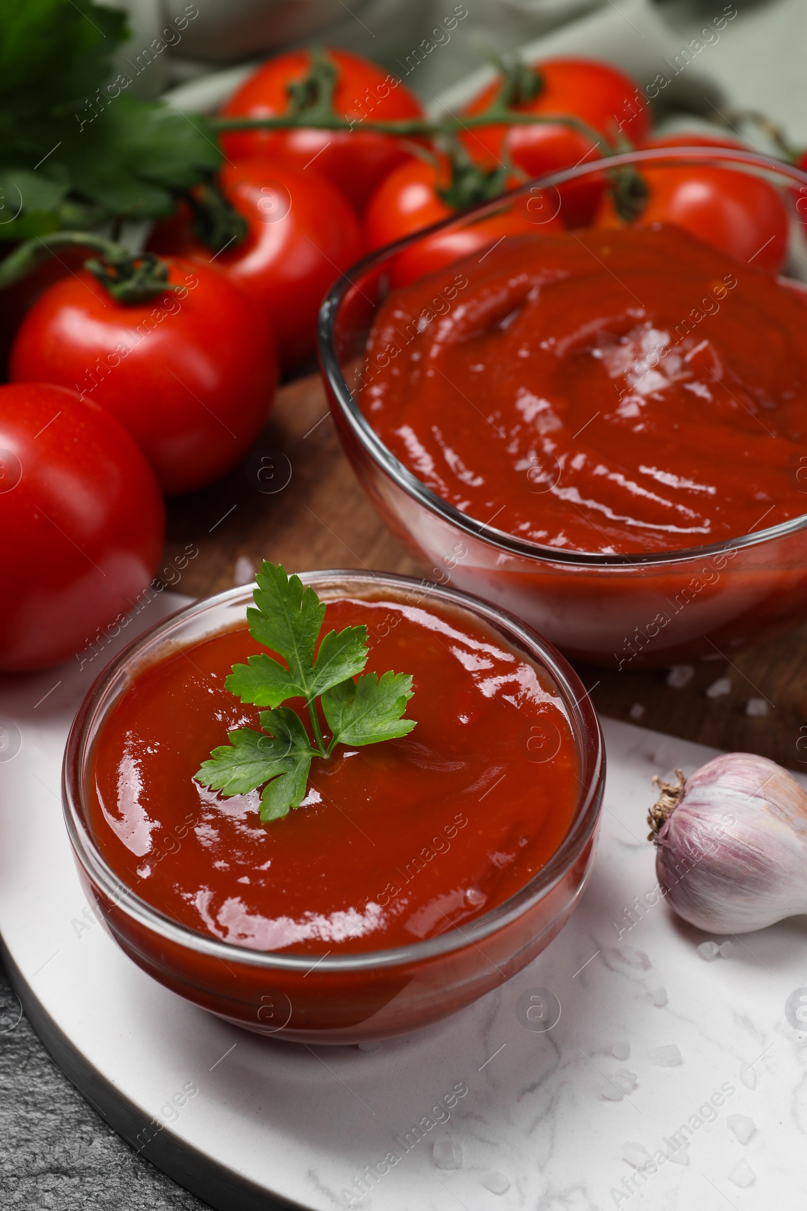 Photo of Organic ketchup in bowls, fresh tomatoes and garlic on table, closeup. Tomato sauce