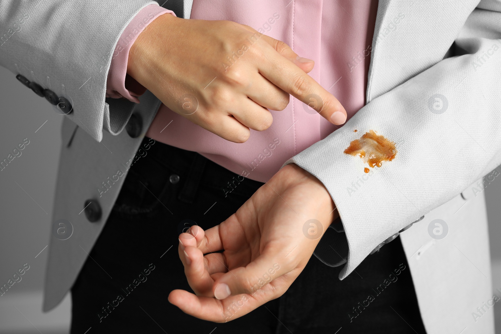 Photo of Woman showing stain of coffee on her jacket against grey background, closeup