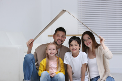 Happy family sitting under cardboard roof at home. Insurance concept