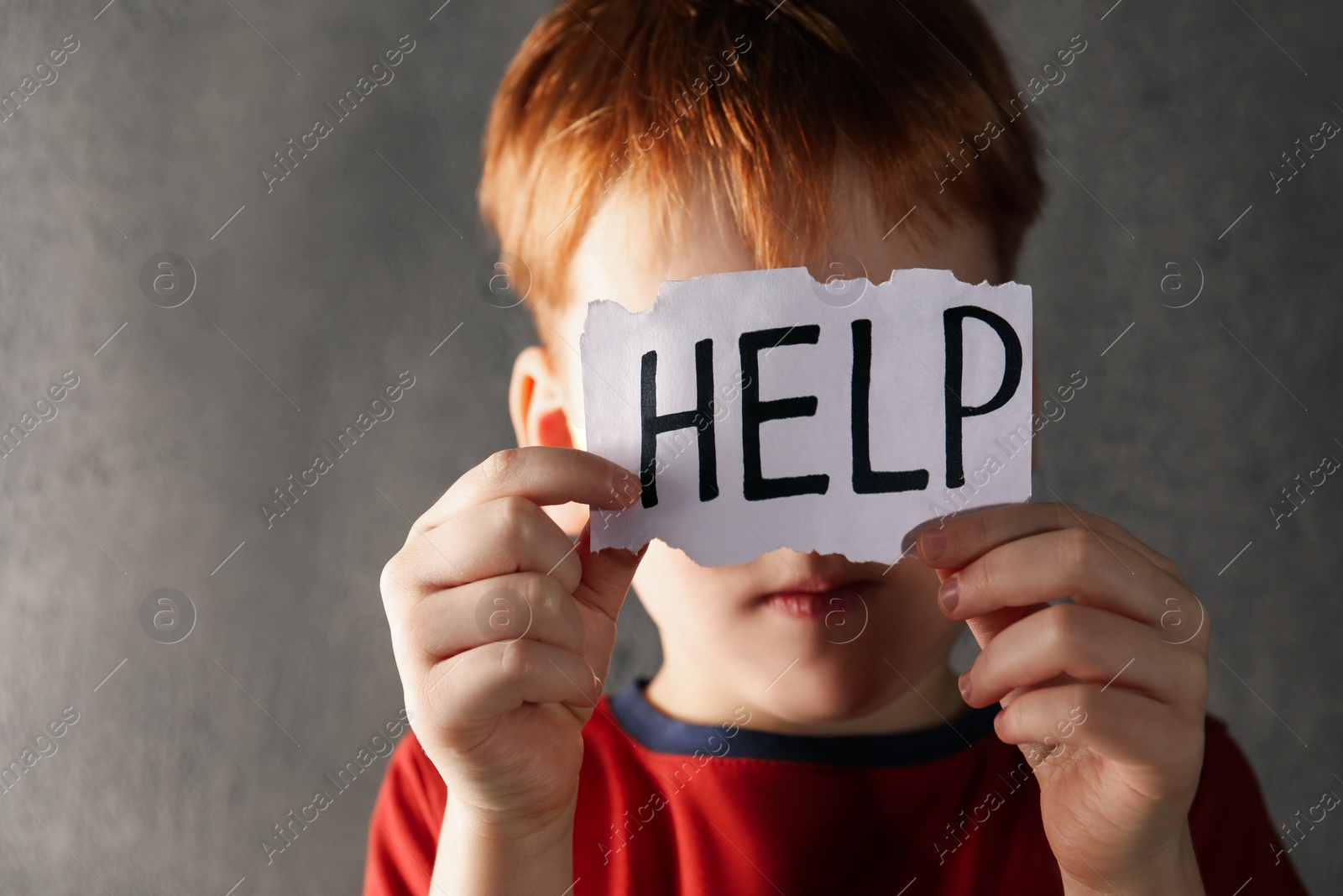 Photo of Little boy holding piece of paper with word Help against light grey background, focus on hands. Domestic violence concept