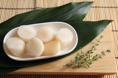 Fresh raw scallops, thyme and green leaves on bamboo mat