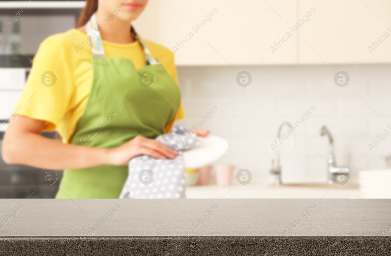 Image of Woman wiping clean dish in kitchen, focus on empty table