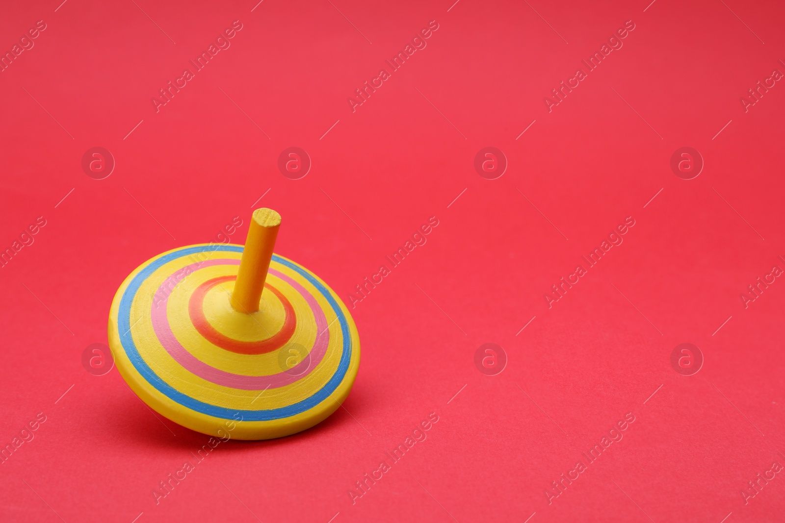 Photo of One bright spinning top on red background, space for text. Toy whirligig