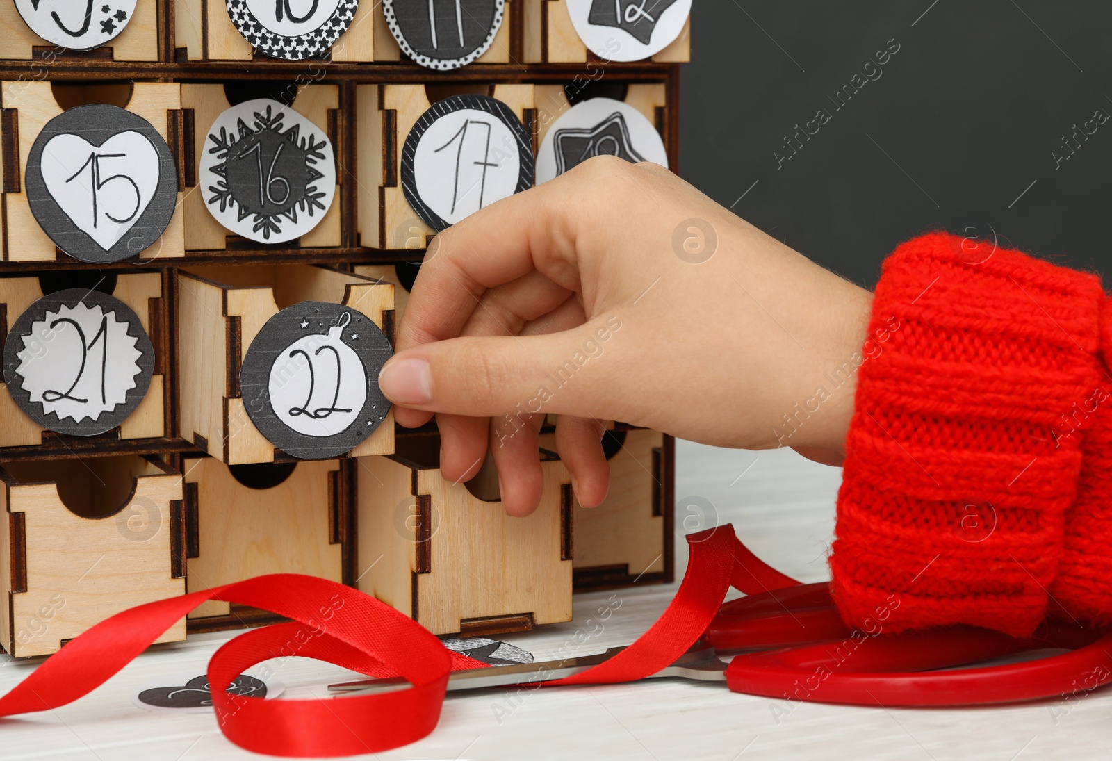 Photo of Woman making advent calendar at white wooden table, closeup