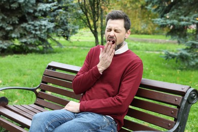 Photo of Sleepy tired man yawning on bench in beautiful green park