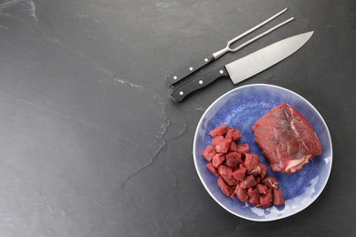 Photo of Plate with pieces of raw beef meat, knife and fork on grey textured table, flat lay. Space for text