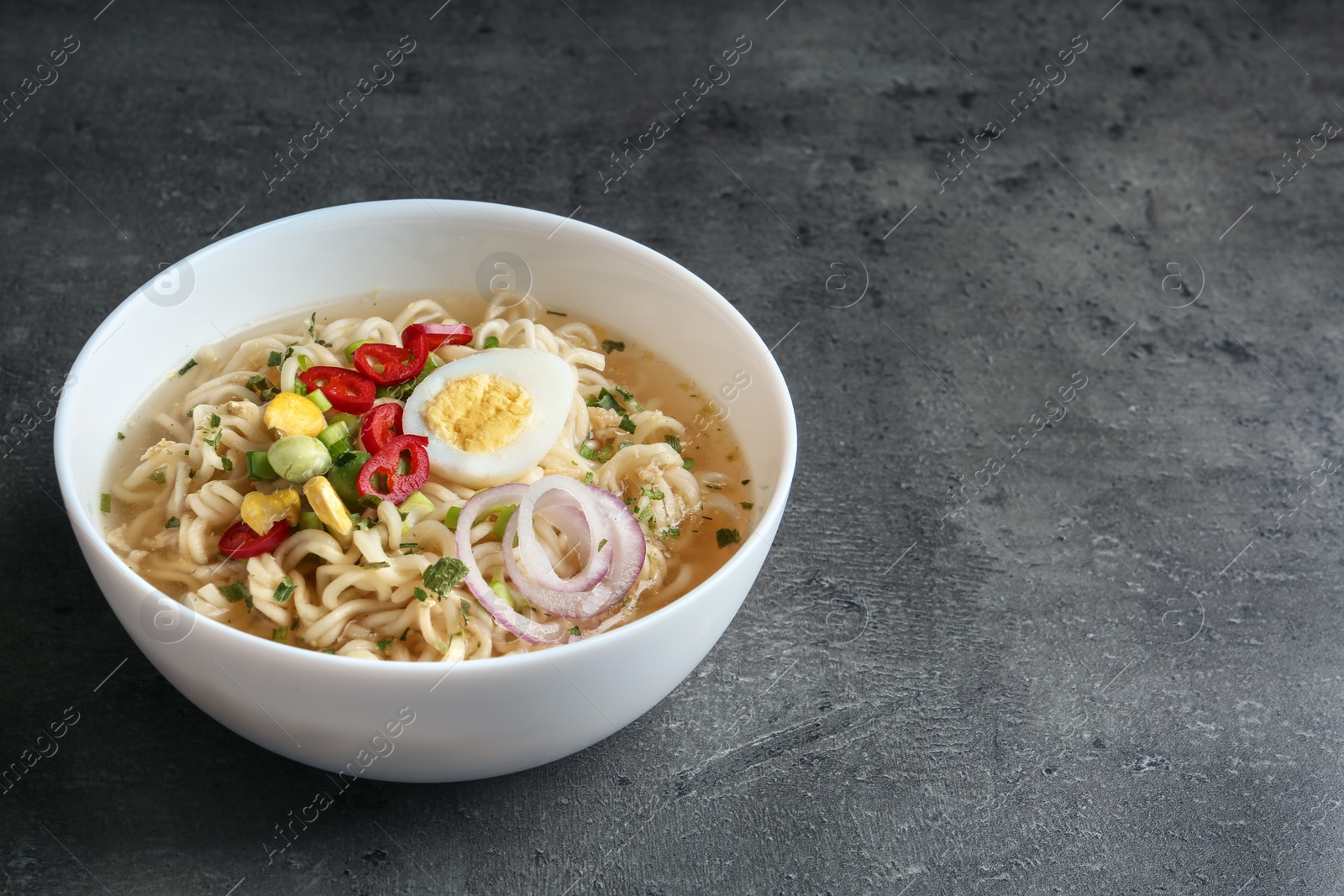 Photo of Bowl of noodles with broth, egg and vegetables on grey background. Space for text