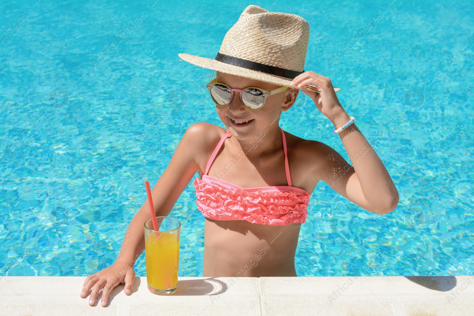 Photo of Cute little girl with glass of juice in swimming pool on sunny day