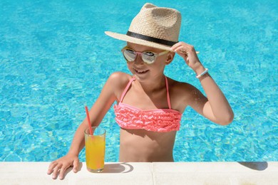 Photo of Cute little girl with glass of juice in swimming pool on sunny day