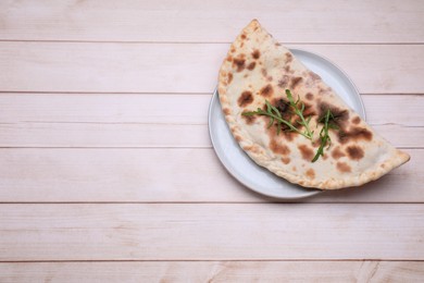 Plate with delicious calzone on light wooden table, top view. Space for text