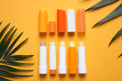 Photo of Sun protection lip balms and leaves on orange background, flat lay