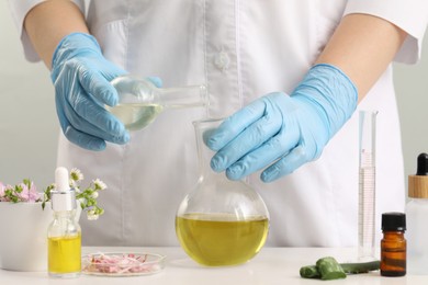 Photo of Scientist developing cosmetic oil at white table, closeup