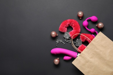 Paper bag with different sex toys and Christmas balls on black background, flat lay. Space for text