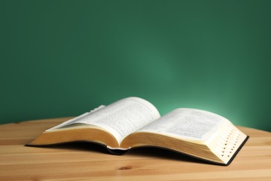 Open Bible on wooden table against green background