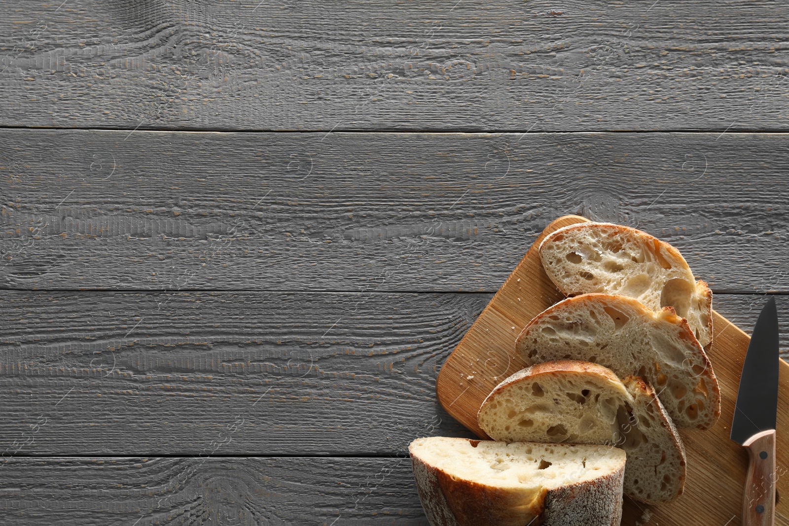 Photo of Food photography. Cut freshly baked bread and knife on wooden table, flat lay with space for text