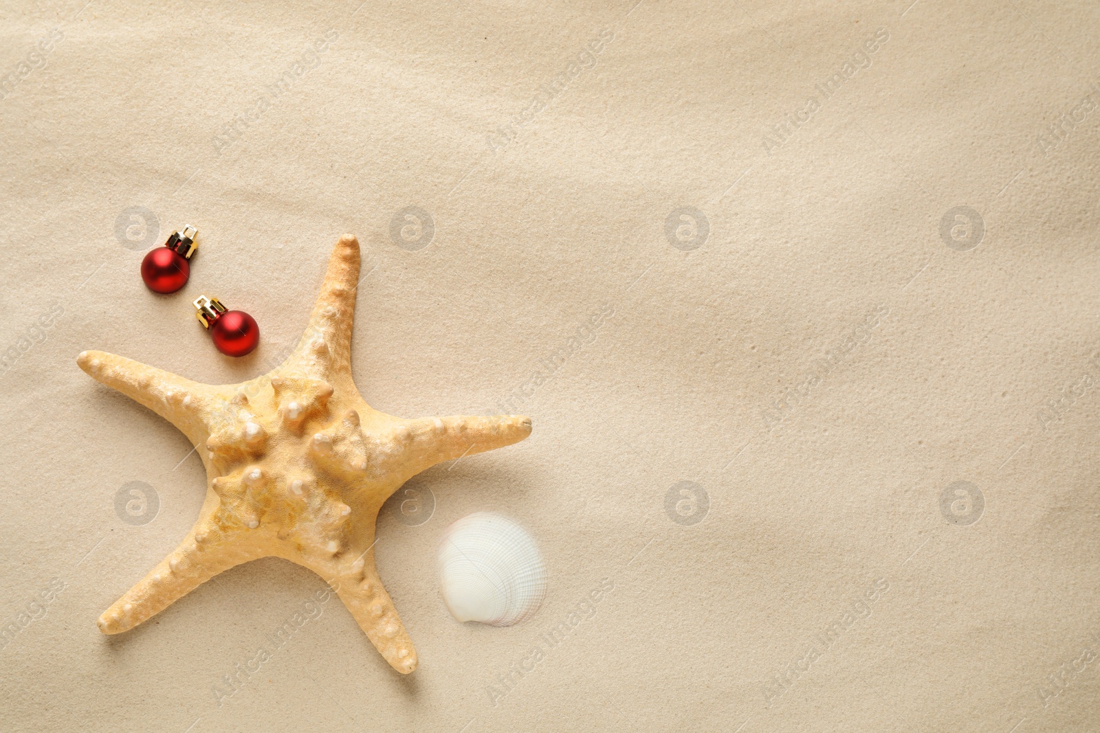 Photo of Beautiful starfish, shell, festive balls and space for text on sand, flat lay. Christmas vacation