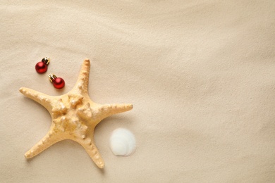 Beautiful starfish, shell, festive balls and space for text on sand, flat lay. Christmas vacation