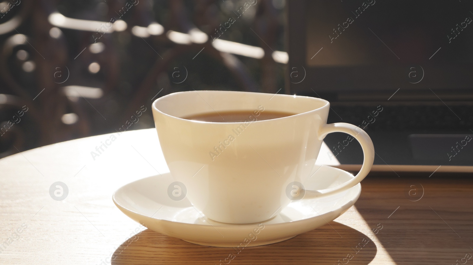 Photo of Cup of aromatic coffee and laptop on wooden table outdoors, closeup