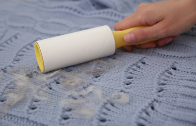 Photo of Woman removing hair from light blue knitted fabric with lint roller, closeup