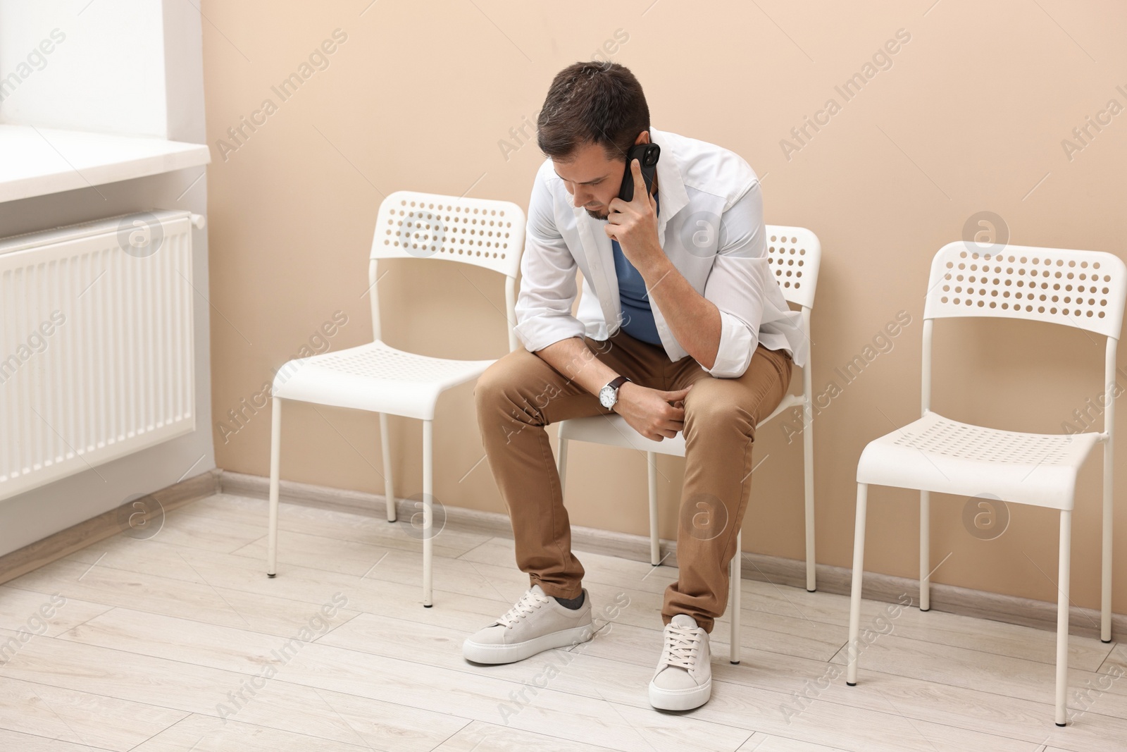 Photo of Man talking on smartphone and waiting for appointment indoors