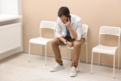 Man talking on smartphone and waiting for appointment indoors