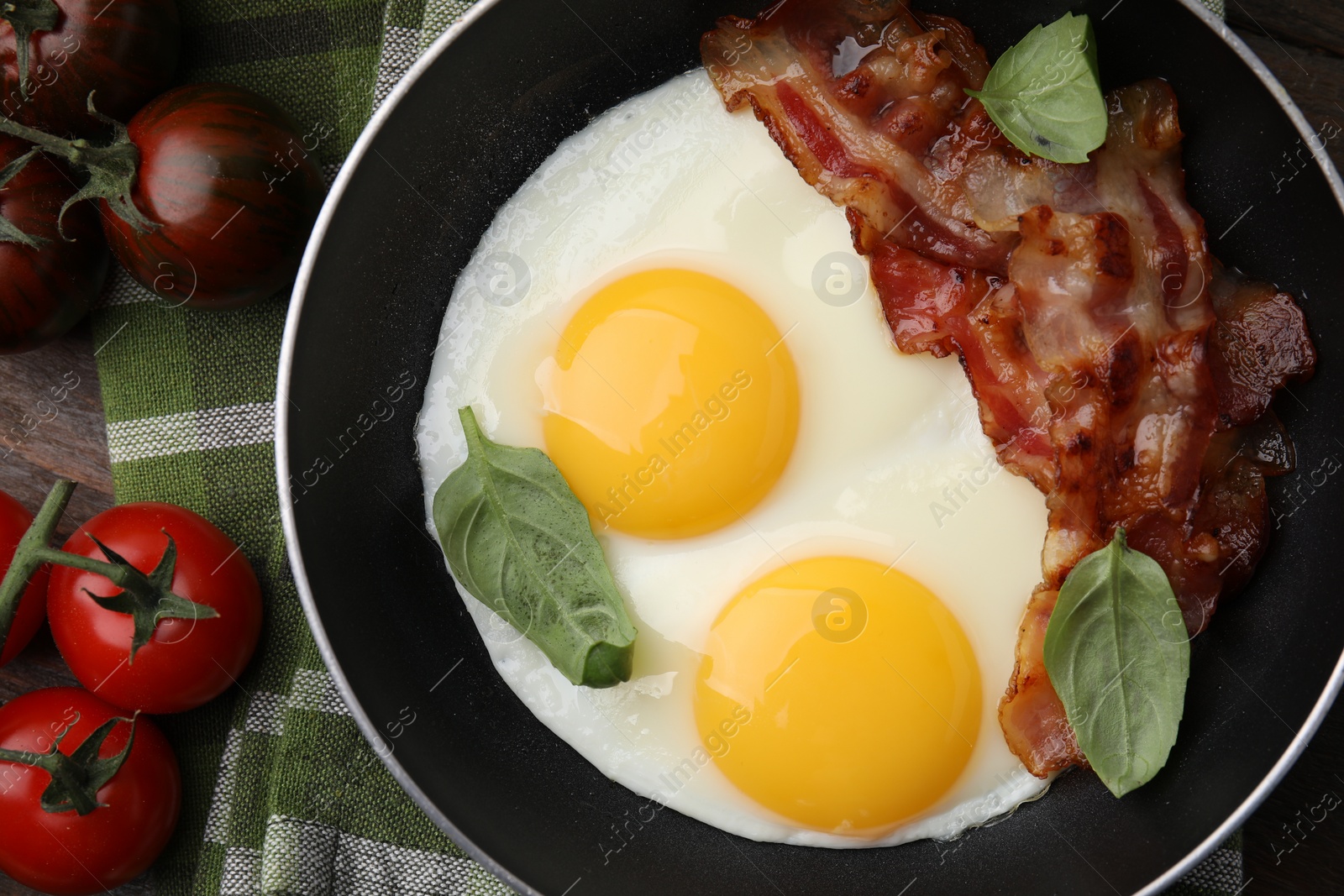 Photo of Fried eggs, bacon, basil and tomatoes on table, top view