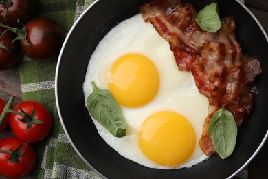 Fried eggs, bacon, basil and tomatoes on table, top view