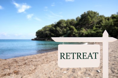 Image of Wooden sign with word Retreat and beautiful view of beach and forest