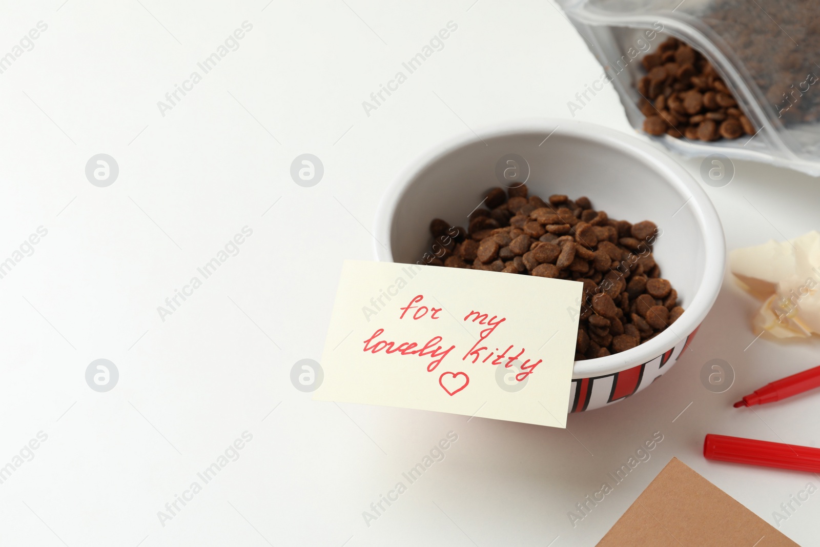 Photo of Composition with dry cat food and cute note on white table. Space for text