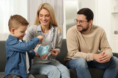 Family budget. Little boy putting coin into piggy bank and his parents at home